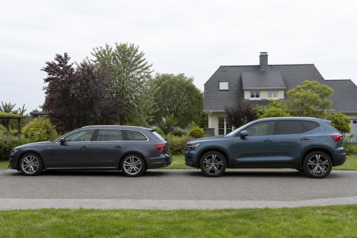 Comparaison de deux véhicules familiaux garés côte à côte devant une maison, l&rsquo;un surélevé et l&rsquo;autre à caisse basse, prise de vue latérale, ciel couvert